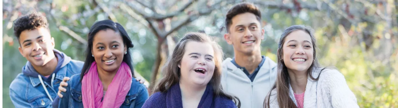 Five young adults smiling together outdoors, representing friendship, inclusion, and peer support.