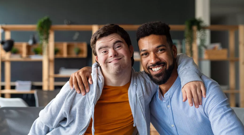 Two men smiling with their arms around each other in an office setting, representing supportive partnership and inclusion.